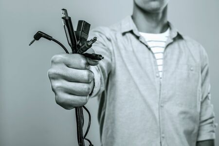 Close up photo of stylish young man standing on grey background holding wires in hand. Black and...