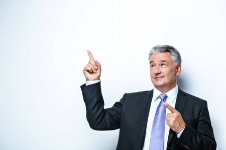 Elderly businessman looking up and pointing at bland wall