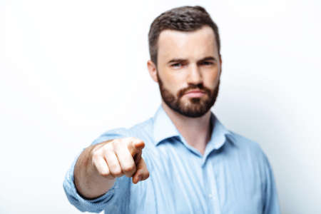 Young businessman with beard on white background seriously looking and pointing at cameraの写真素材