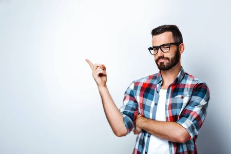 Stylish man wearing glasses, looking at camera and pointing at bland wallの写真素材