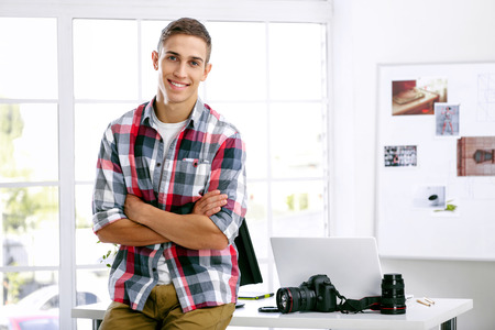 Professional photographer with camera and laptop computer in office, looking in the camera and...
