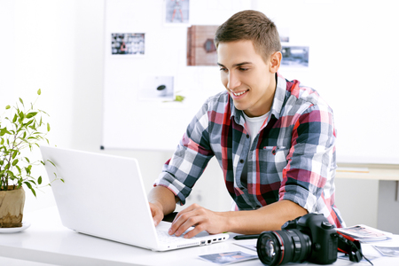 Professional photographer with camera, graphics tablet and laptop computer working in office, looking at monitor and smilingの写真素材