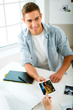 Professional photographer with camera, graphics tablet and laptop computer working in office, he giving a photo to personの写真素材