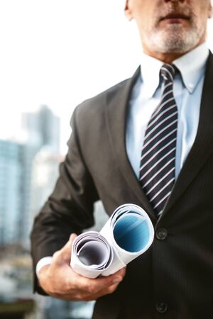 Business portrait of contractor and developer. Aged businessman standing near his new construction and holding blueprintsの写真素材