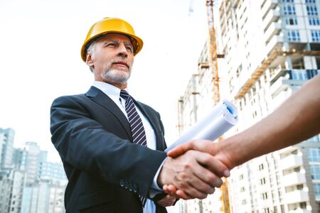 Portrait of engineer and builder. Men with helmet standing near new unfinished construction. Men shaking hands after dealの写真素材