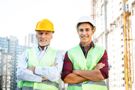 Portrait of contractor and builder in uniforms. Men with helmets standing near new unfinished construction and looking at cameraの写真素材
