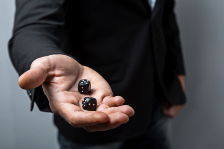 Studio shot of young man's hand on grey background. Man wearing jacket and shirt. Man showing diceの写真素材