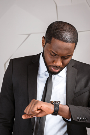 Portrait of handsome afro american businessman. Young stylish businessman looking at watch. Man wearing suit and tieの写真素材