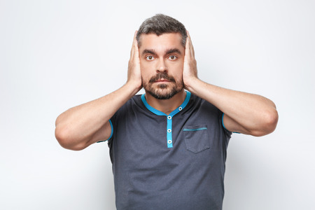 Portrait of handsome caucasian man with grey beard standing on white background. Man covering his ears with handsの写真素材