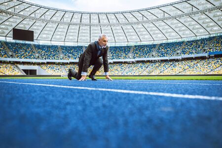 Side view photo of confident aged businessman lined up getting ready for race on modern sport track. Stadium as a backgroundの写真素材