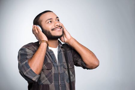 Young mixed race man with beard standing on grey background. Young man smiling and listening to music with headphonesの写真素材