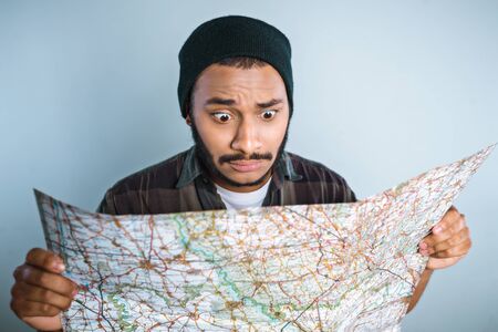Young mixed race man with beard and map standing on grey backgroundの写真素材