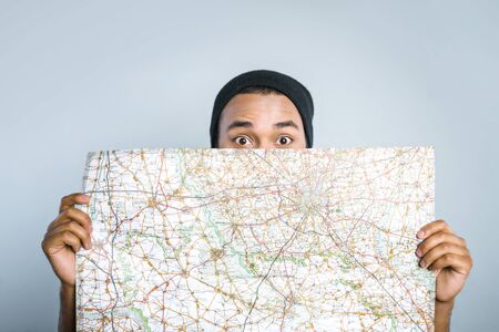 Young mixed race man with map standing on grey backgroundの写真素材