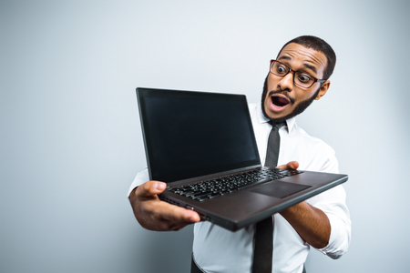 Fun picture of young mixed race businessman with beard standing on grey background. Young man holding laptopの写真素材