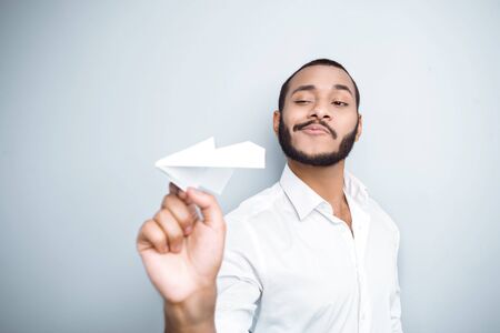Young mixed race man with beard standing on grey background. Young man starting up paper planeの写真素材