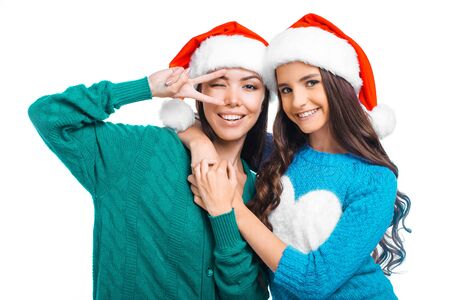Christmas portrait of beautiful two mixed-race girls. Teenagers wearing santa claus hats. Girls smiling and looking at cameraの写真素材