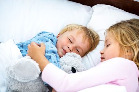 Photo of little girl and boy sleeping on white bed. Sister and brother huggingの写真素材