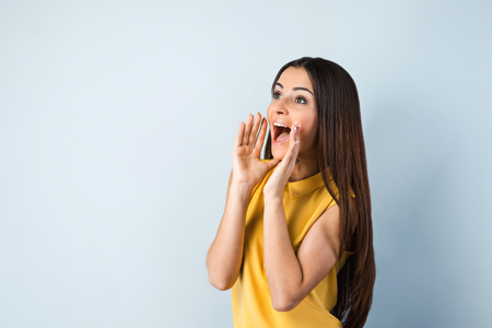 Photo of beautiful young business woman standing near gray background. Woman with yellow shirt looking and screaming asideの写真素材