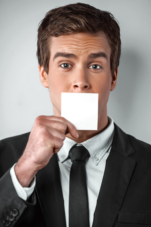 Studio shot of young handsome businessman. Businessman looking at camera and hiding mouth behind visit cardの写真素材