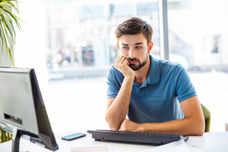 Photo of young, handsome, successful and confident businessman. Young businessman is bored while working with computer. White modern office interiorの写真素材