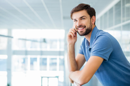 Portrait of young businessman. Smiling man using mobile phone and standing in nice modern building. Office interiorの写真素材