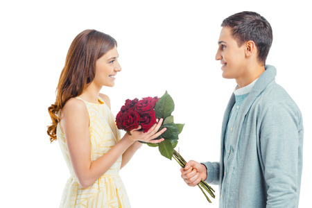 Romantic photo of beautiful couple on white background. Handsome young man giving red roses to his girlfriendの写真素材