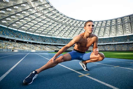 Young handsome sportsman stretching outdoors. Fit sporty man is at large nice modern stadiumの写真素材