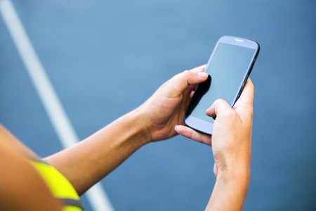 Close up photo of young sportswoman on racetrack outdoors. Fit woman using mobile phoneの写真素材