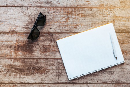 Creative horizontal top view photo of business objects on light colored woodblocks. There are notebook, sunglasses and penの写真素材