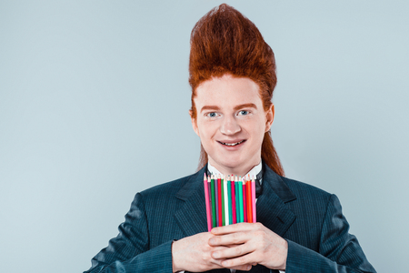 Stylish redheaded young man with bouffant on head. Boy wearing suit with bow-tie, holding colorful stickers and looking at cameraの写真素材