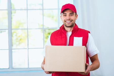 Delivery service worker in uniform delivering parcel. Man with box smiling and looking at camera