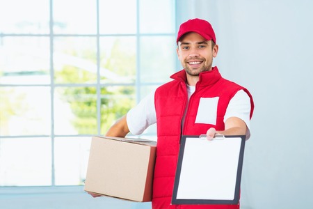 Delivery service worker in uniform delivering parcel. Man with box proposing document to sign and looking at cameraの写真素材