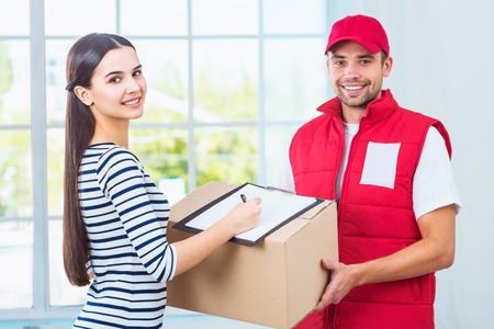 Delivery service worker in uniform delivering parcel to woman. Happy woman signing document and looking at cameraの写真素材