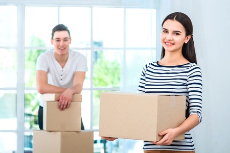 Happy couple smiling, packing and closing carton box. Focus on woman. Woman holding box and looking at cameraの写真素材