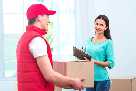 Delivery service worker in uniform delivering parcel to woman. Woman signing document and looking at cameraの写真素材