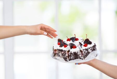 Close up photo of female hand reaching to chocolate cake in kitchenの写真素材