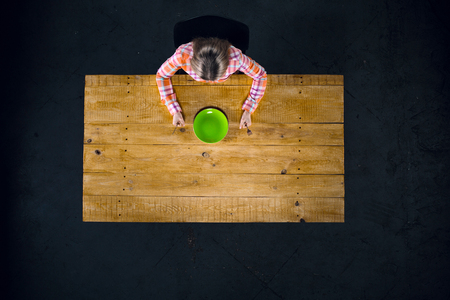Top view creative photo of girl sitting at wooden vintage table. Girl with empty green plateの写真素材