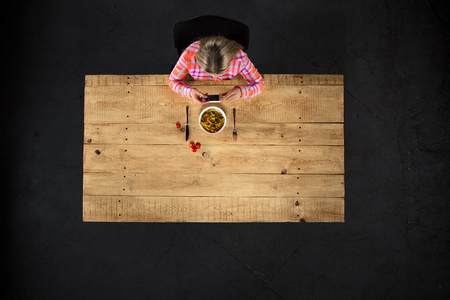Top view creative photo of girl sitting at wooden vintage table. Girl with plate full of delicious meal. Girl using mobile phoneの写真素材