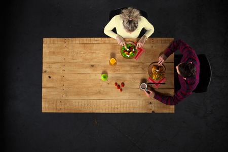 Top view creative photo of couple sitting at wooden vintage table. Man and woman having romantic dinner. They with plates full of delicious meal and glasses with wineの写真素材