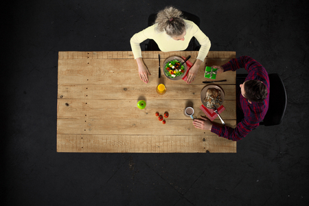 Top view creative photo of couple sitting at wooden vintage table. Man and woman having romantic dinner. They with plates full of delicious meal and glasses with wine. Man presenting gift to womanの写真素材