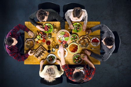 Top view creative photo of friends sitting at wooden vintage table. Friends of six having dinner. They with plates full of delicious meal and glasses with drinksの写真素材