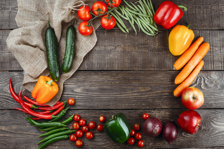 Top view studio shot of fresh vegetables on wooden table. Empty space for logo on center. There are onion, apple, pepper, hot pepper, cucumber, tomato, carrot, green peasの写真素材