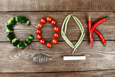 Top view studio shot of fresh vegetables on wooden table. There are vegetables in shape of word "cook"の写真素材