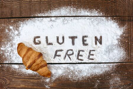 Top view studio shot of gluten-free word with flour and croissant on wooden tableの写真素材