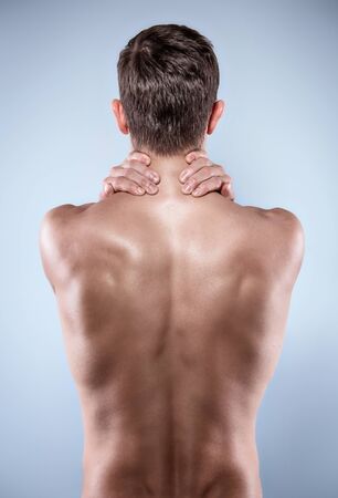 Studio shot of handsome young man with naked torso. Man suffering from neck ache. Back view photoの写真素材