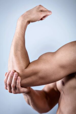 Studio shot of handsome young man with naked torso. Man suffering from arm acheの写真素材