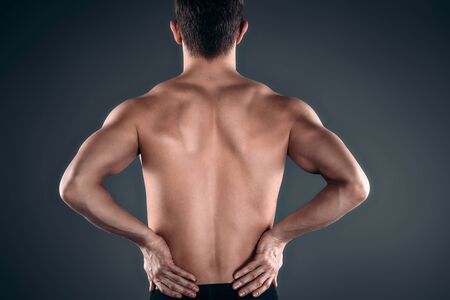 Studio shot of handsome young man with naked torso. Man suffering from backache
