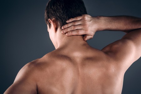 Studio shot of handsome young man with naked torso. Man suffering from neck acheの写真素材