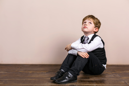 Little boy wearing school uniform. Boy sitting at wooden floor and dreamingの写真素材