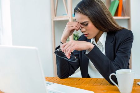 Beautiful young business woman in modern office. Tired woman with headache working with laptopの写真素材